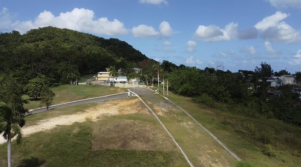 An aerial view shows a paved road leading toward a house nestled against a green hill — HACIENDA RIO LAJAS UNIT #1, DORADO, PR