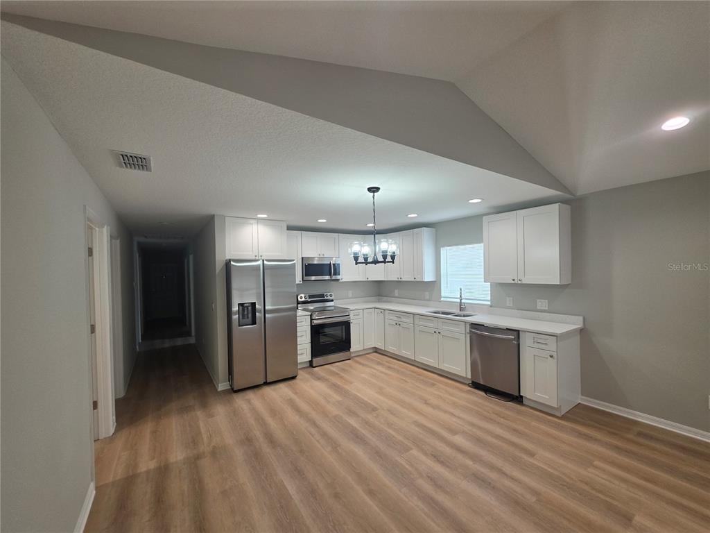 A kitchen features white cabinets, stainless steel appliances, and light wood-look flooring under vaulted ceilings — 851 AVENUE R NE, WINTER HAVEN, FL