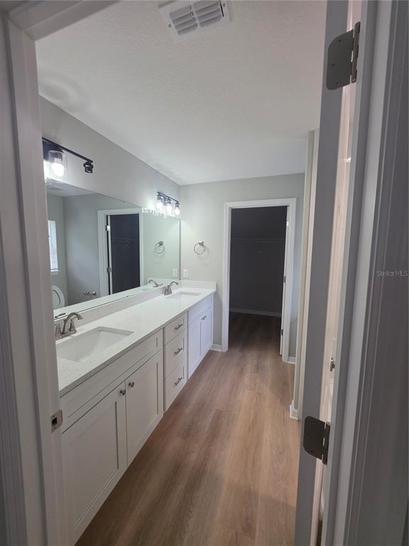 A bathroom features a double vanity with white cabinets, quartz countertops, and wood-look flooring — 851 AVENUE R NE, WINTER HAVEN, FL