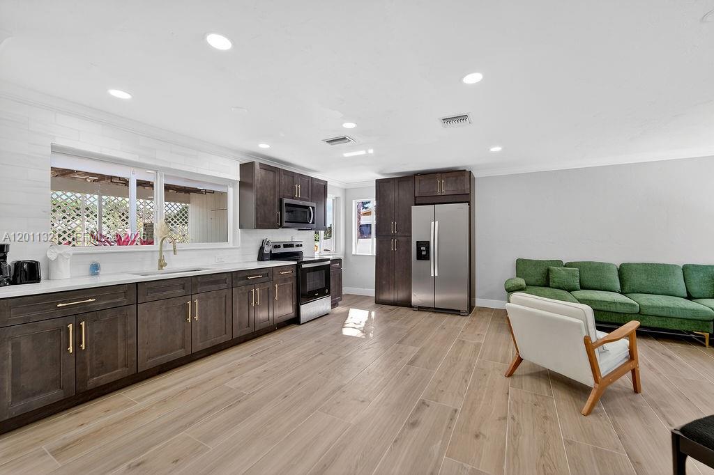 A kitchen with dark wood cabinets and stainless steel appliances opens to a living area — 756 Cinnamon Rd, North Palm Beach FL 33408, NORTH PALM BEACH, FL