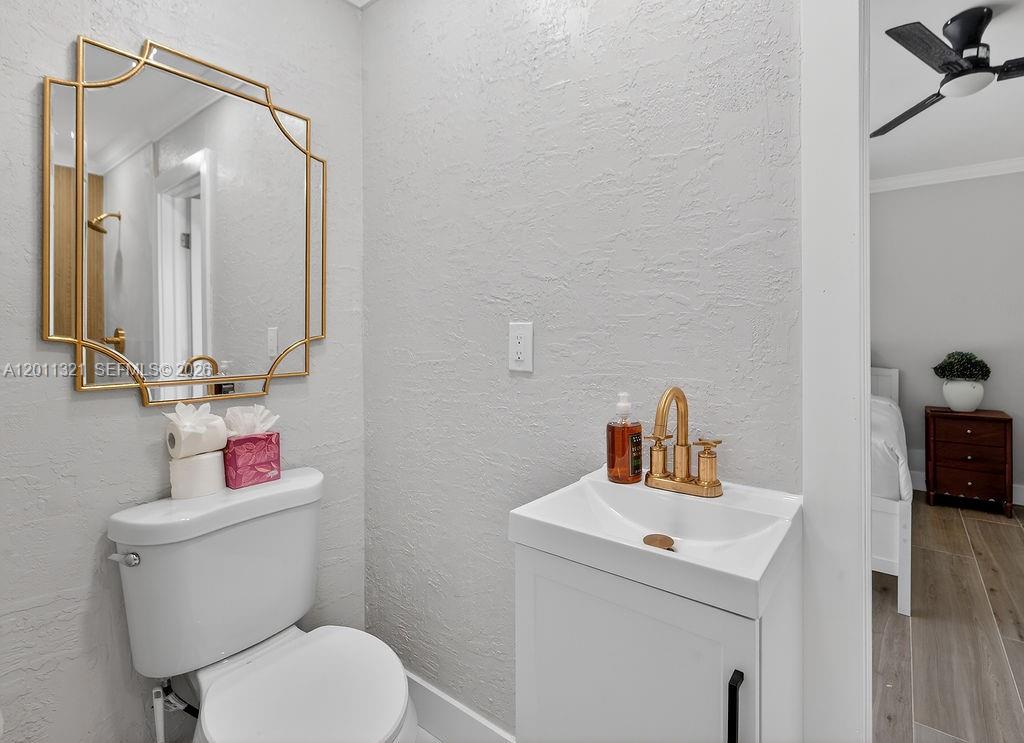 A small bathroom features a white pedestal sink, a toilet, and a gold-framed mirror — 756 Cinnamon Rd, North Palm Beach FL 33408, NORTH PALM BEACH, FL
