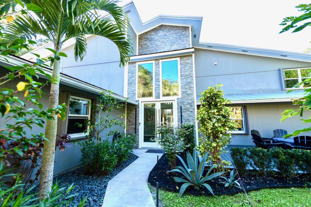 A modern house exterior features a stone-accented entryway, a concrete walkway, and lush landscaping — 16887 97th Way N, Jupiter FL 33478, JUPITER, FL