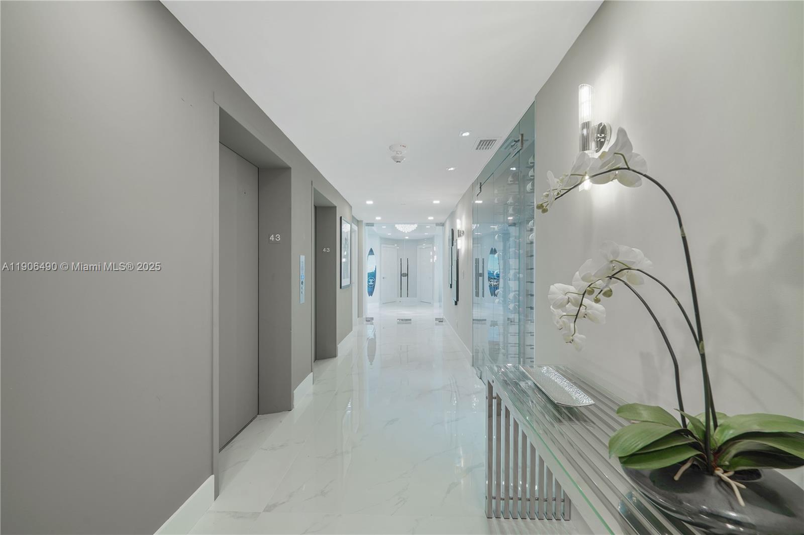 A modern hallway features gray walls, marble flooring, elevator doors, and a glass-enclosed wine display — 300 S Pointe Dr # 4306, Miami Beach FL 33139, MIAMI BEACH, FL
