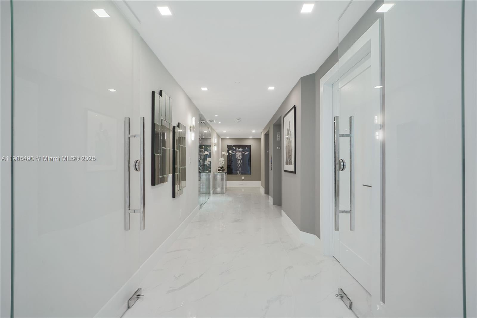 A modern, brightly lit hallway features white marble floors, glass doors, and gray accent walls — 300 S Pointe Dr # 4306, Miami Beach FL 33139, MIAMI BEACH, FL