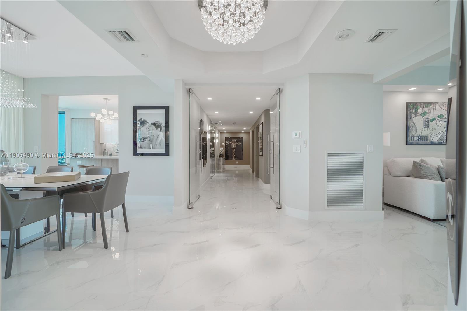 A bright, modern interior features white marble floors, a crystal chandelier, and a glass-enclosed hallway — 300 S Pointe Dr # 4306, Miami Beach FL 33139, MIAMI BEACH, FL