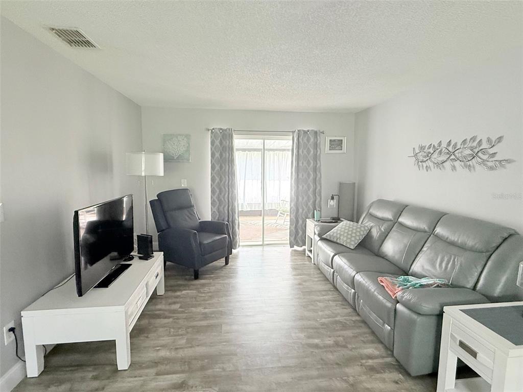 A living room features light gray walls, wood-look flooring, a gray sofa, and a television — 3357 38TH STREET S UNIT C, ST PETERSBURG, FL