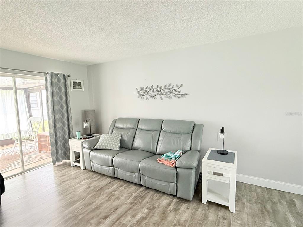 A living room features a gray leather sofa, two white end tables, and wood-look flooring — 3357 38TH STREET S UNIT C, ST PETERSBURG, FL