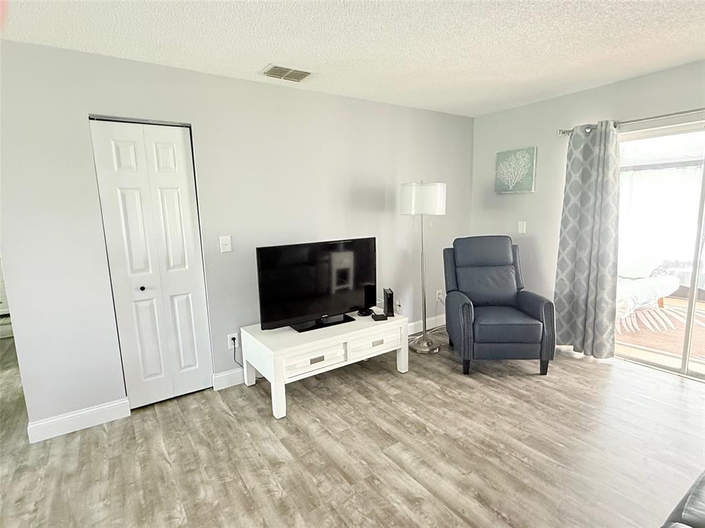 A living room features light gray walls, wood-look flooring, a television stand, and a recliner — 3357 38TH STREET S UNIT C, ST PETERSBURG, FL