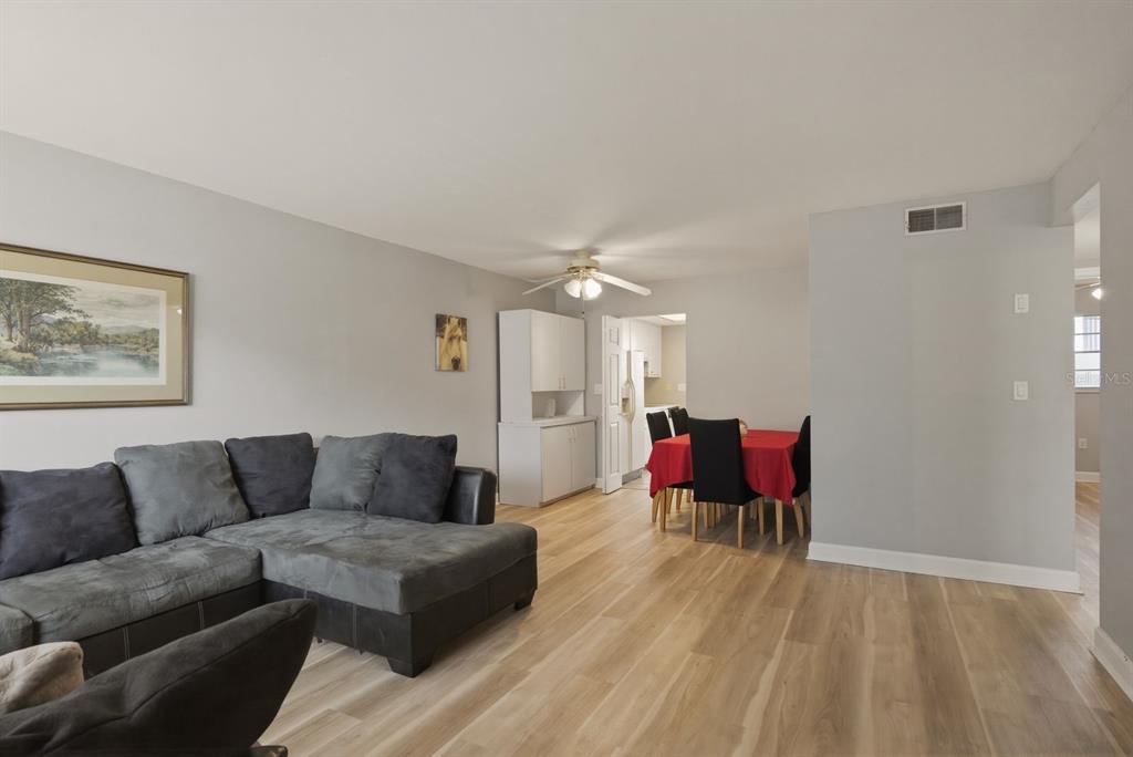 A living room with light wood floors, a grey sectional sofa, and a dining area — 2011 58TH AVENUE N UNIT 5, ST PETERSBURG, FL