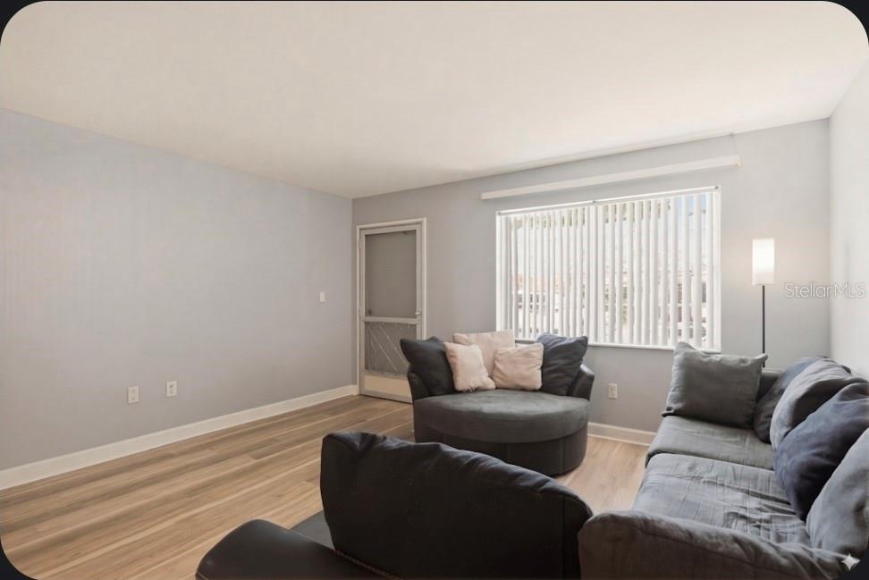 A living room features light gray walls, wood-look flooring, a window with blinds, and furniture — 2011 58TH AVENUE N UNIT 5, ST PETERSBURG, FL