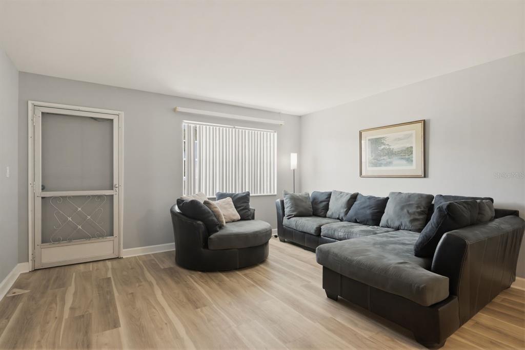 A living room features light gray walls, wood-look flooring, a sectional sofa, and a round chair — 2011 58TH AVENUE N UNIT 5, ST PETERSBURG, FL