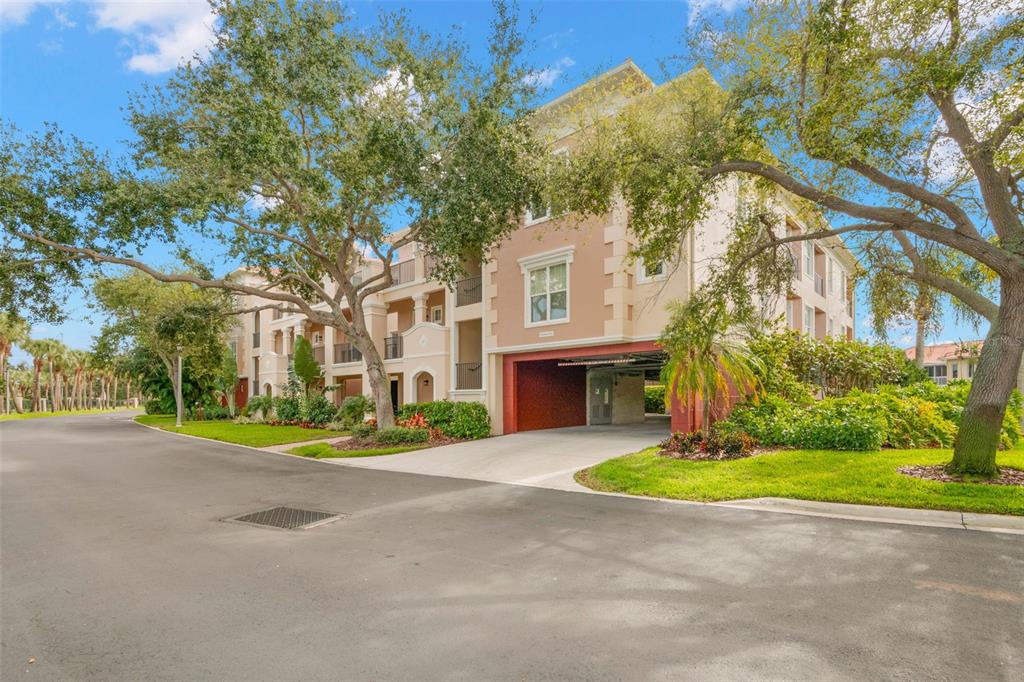A multi-story apartment building with a ground-level parking garage and surrounding trees and landscaping — 8 ACADEMY WAY S UNIT 123, ST PETERSBURG, FL