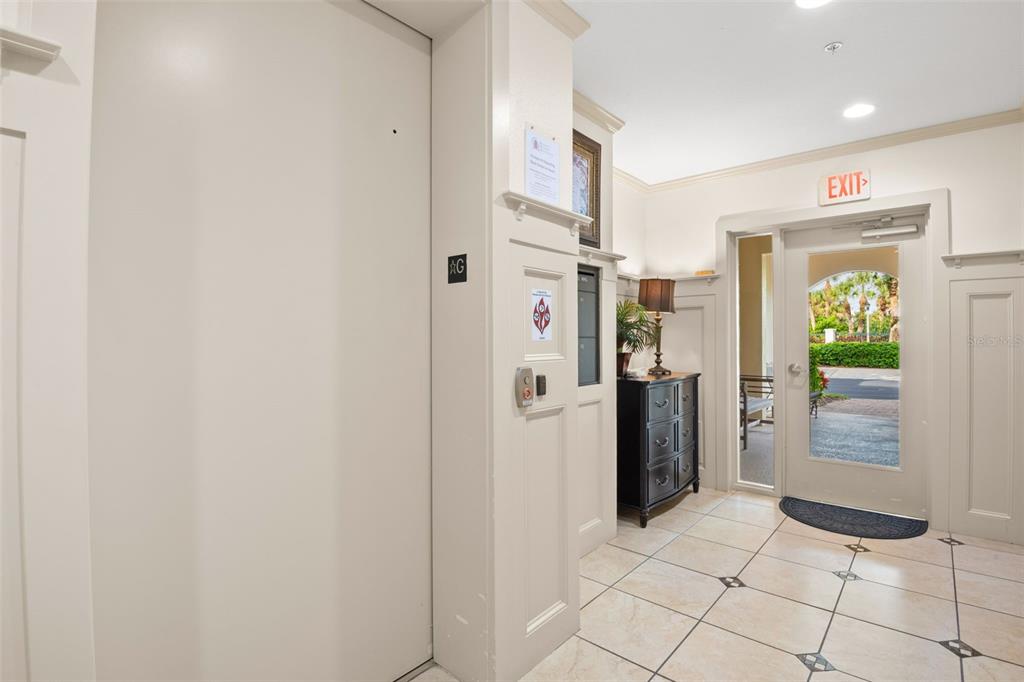 A building lobby features a white elevator, a dark chest, and a glass exit door — 8 ACADEMY WAY S UNIT 123, ST PETERSBURG, FL