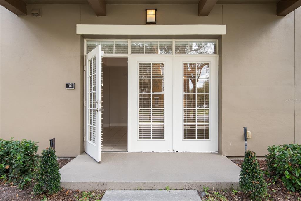 A ground-level apartment entrance features a concrete porch, white French doors, and unit number 102 — 1410 CELEBRATION AVENUE UNIT #102, CELEBRATION, FL