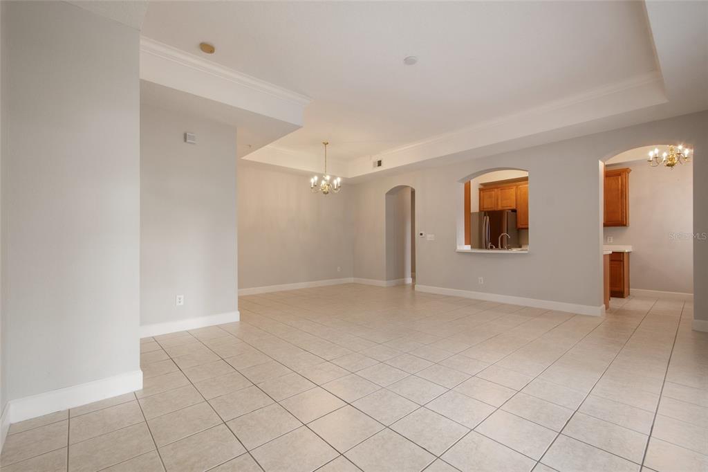 An empty room with light-colored tile flooring, neutral walls, and a pass-through to the kitchen — 1410 CELEBRATION AVENUE UNIT #102, CELEBRATION, FL