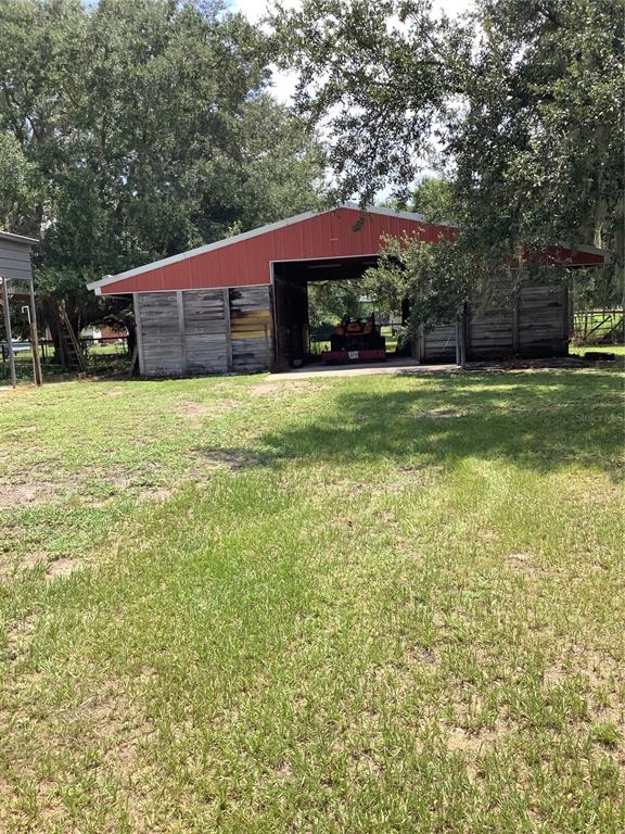 A red-roofed barn with weathered wooden siding stands in a grassy, tree-shaded yard — 3845 CHAPLAIN ROAD, ST CLOUD, FL
