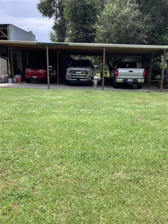 A large metal carport shelters three vehicles parked on a concrete slab beside a lawn — 3845 CHAPLAIN ROAD, ST CLOUD, FL