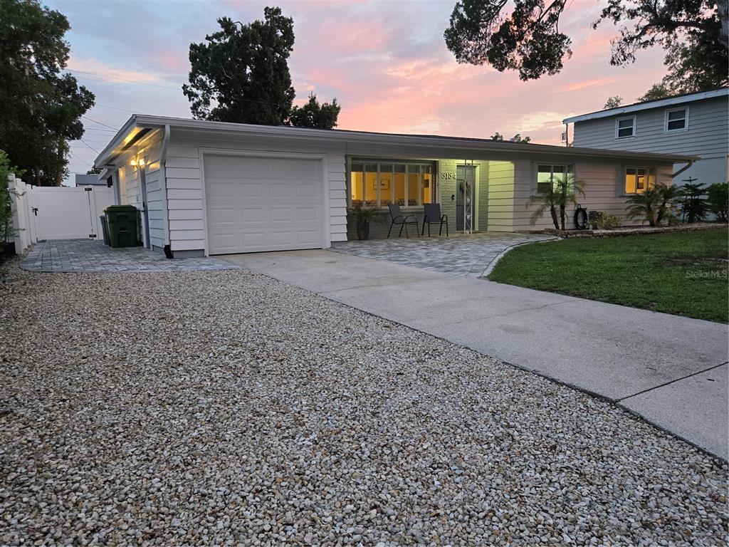 A single-story house with a white exterior, gravel driveway, and a paved walkway at sunset — 3134 IRVING STREET, SARASOTA, FL
