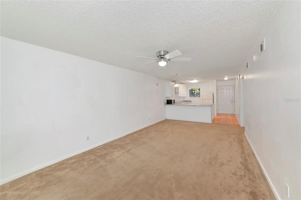 A spacious living room with beige carpeting leads to an open kitchen with white cabinets — 6033 34TH STREET W UNIT 58, BRADENTON, FL