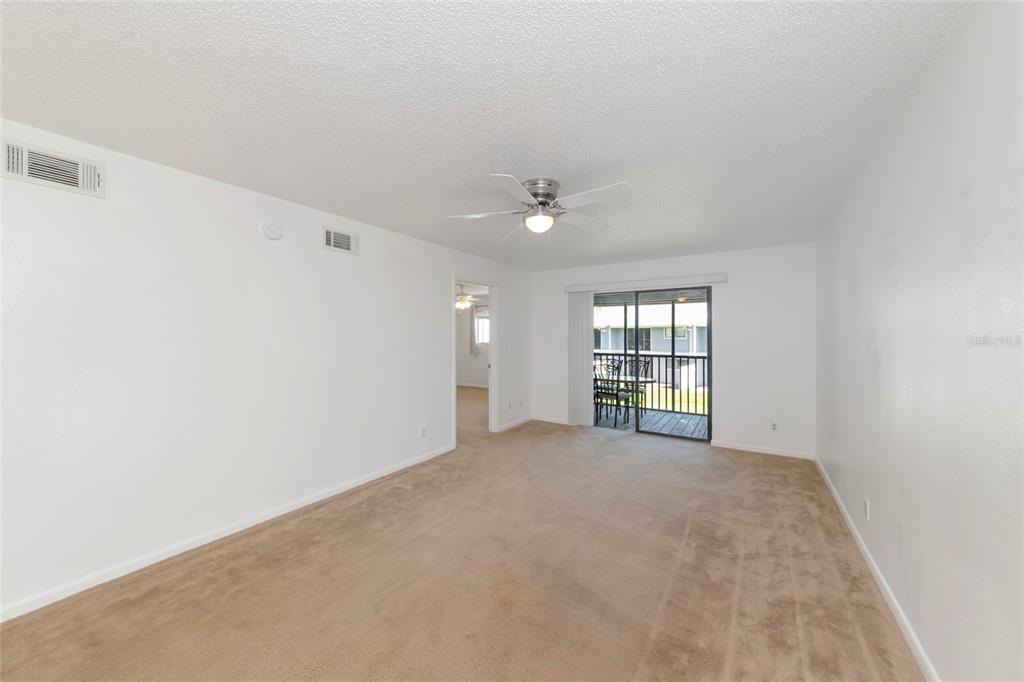 A living room with beige carpet, white walls, a ceiling fan, and a sliding glass door — 6033 34TH STREET W UNIT 58, BRADENTON, FL