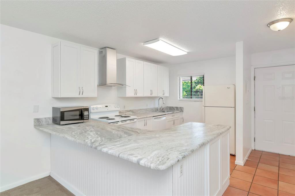 A kitchen with white cabinets, stone countertops, stainless steel appliances, and a tiled floor — 6033 34TH STREET W UNIT 58, BRADENTON, FL