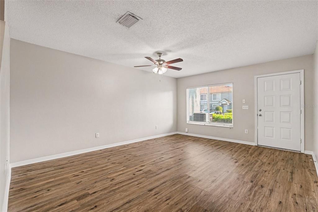 An empty living room features light-colored walls, wood-look flooring, a ceiling fan, and a window — 2125 FLUORSHIRE DRIVE, BRANDON, FL