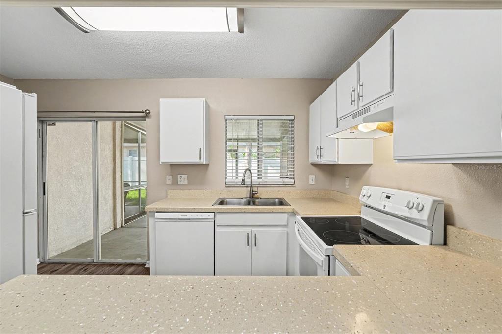 A kitchen with white cabinets, speckled countertops, stainless steel sink, and a sliding glass door — 2125 FLUORSHIRE DRIVE, BRANDON, FL
