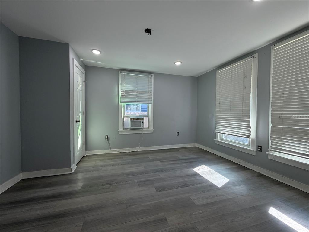An empty room with gray walls, wood-look flooring, three windows with blinds, and a door — 335 MAPLE STREET, DAYTONA BEACH, FL