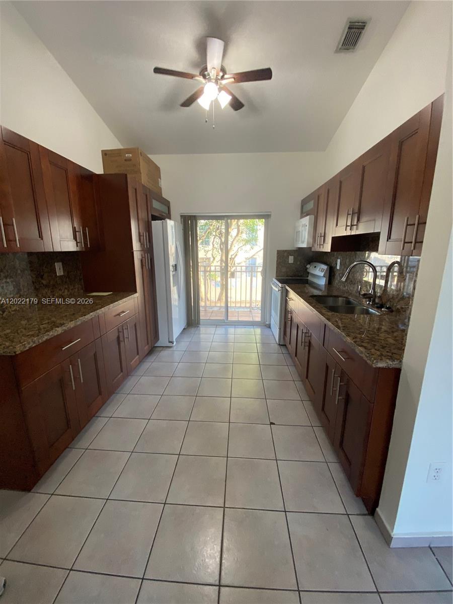A galley kitchen features dark wood cabinets, granite countertops, tile flooring, and a sliding glass door — 7500 W 20th Ave # 202, Hialeah FL 33016, HIALEAH, FL