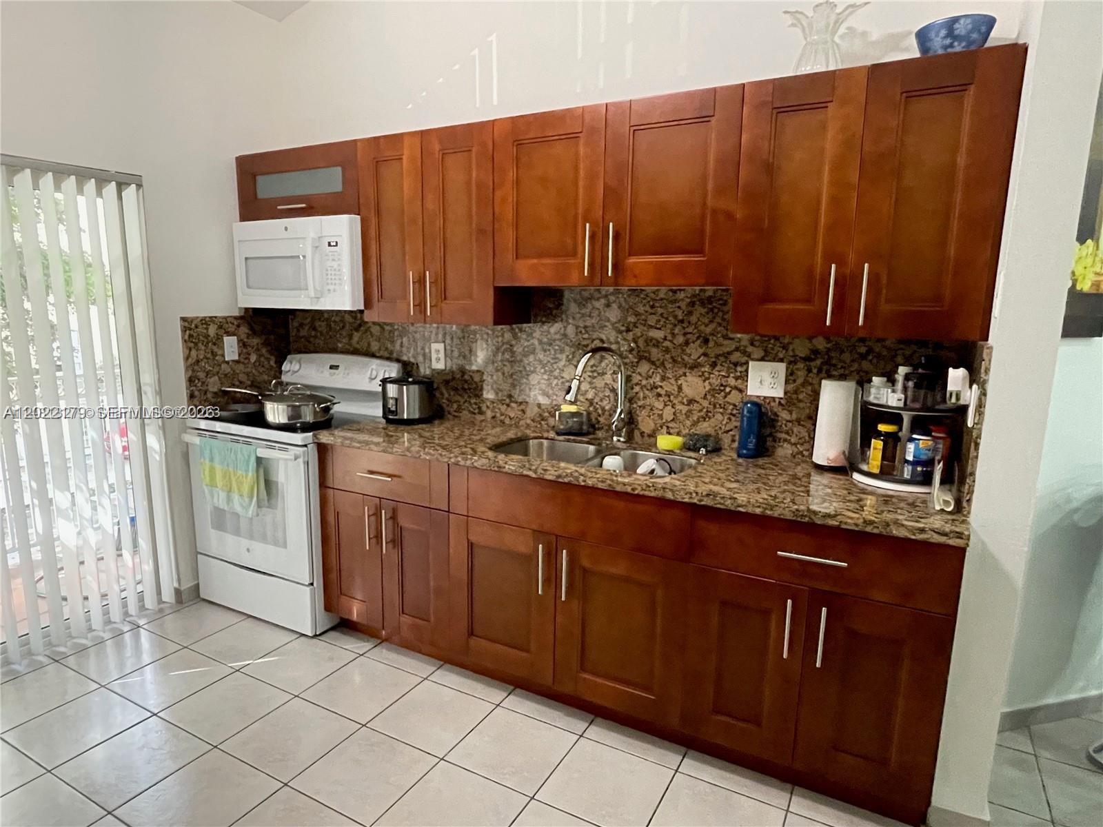 A kitchen features wood cabinets, granite countertops, a white stove, and a double sink — 7500 W 20th Ave # 202, Hialeah FL 33016, HIALEAH, FL