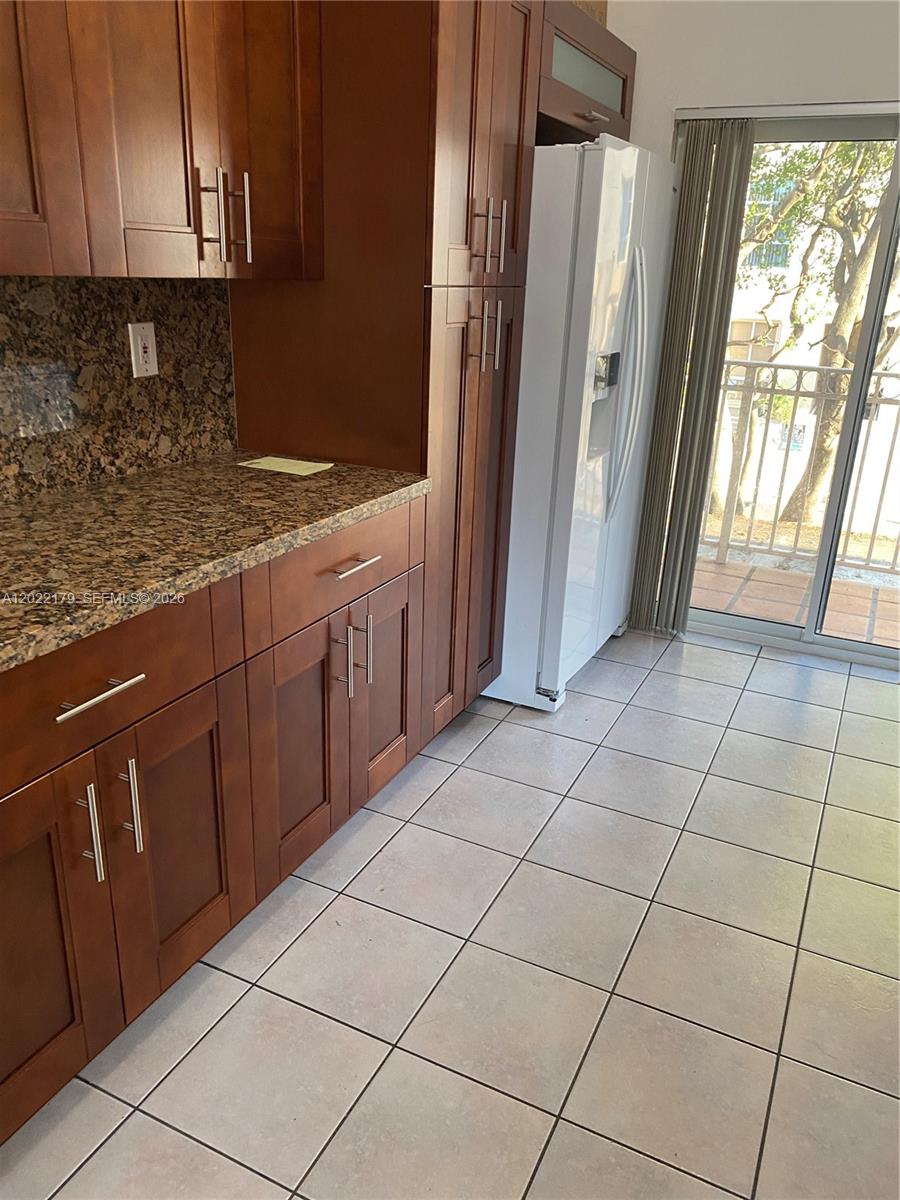 A kitchen features dark wood cabinets, granite countertops, a white refrigerator, and tile flooring — 7500 W 20th Ave # 202, Hialeah FL 33016, HIALEAH, FL