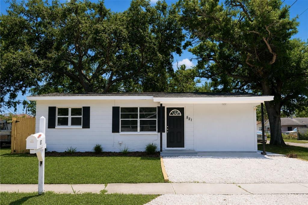 A single-story white house with black shutters, a black front door, and a gravel driveway — 821 14TH AVENUE NW, LARGO, FL