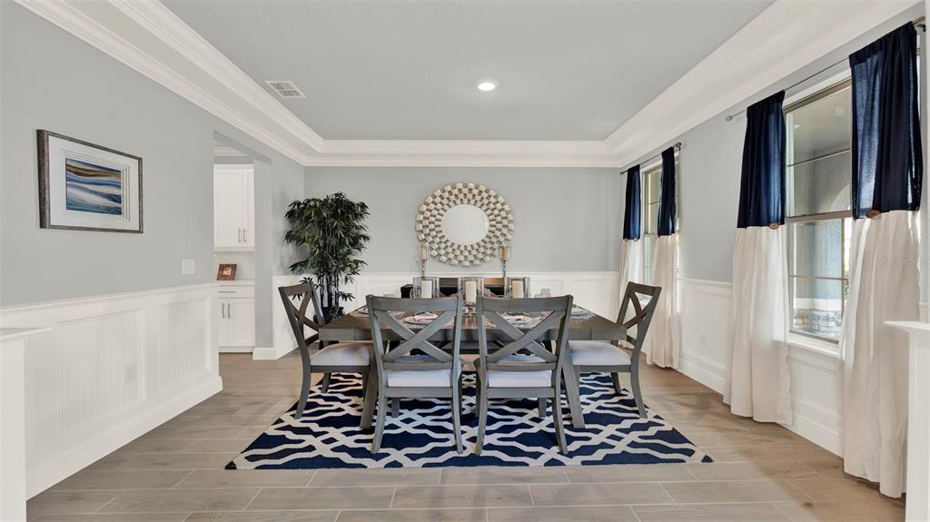 A dining room features a wooden table, six chairs, a patterned rug, and wainscoting — 11259 HOLLOW BAY DRIVE, WINTER GARDEN, FL