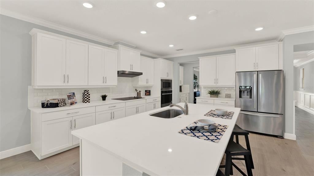 A modern kitchen features white cabinetry, a large central island, and stainless steel appliances — 11259 HOLLOW BAY DRIVE, WINTER GARDEN, FL