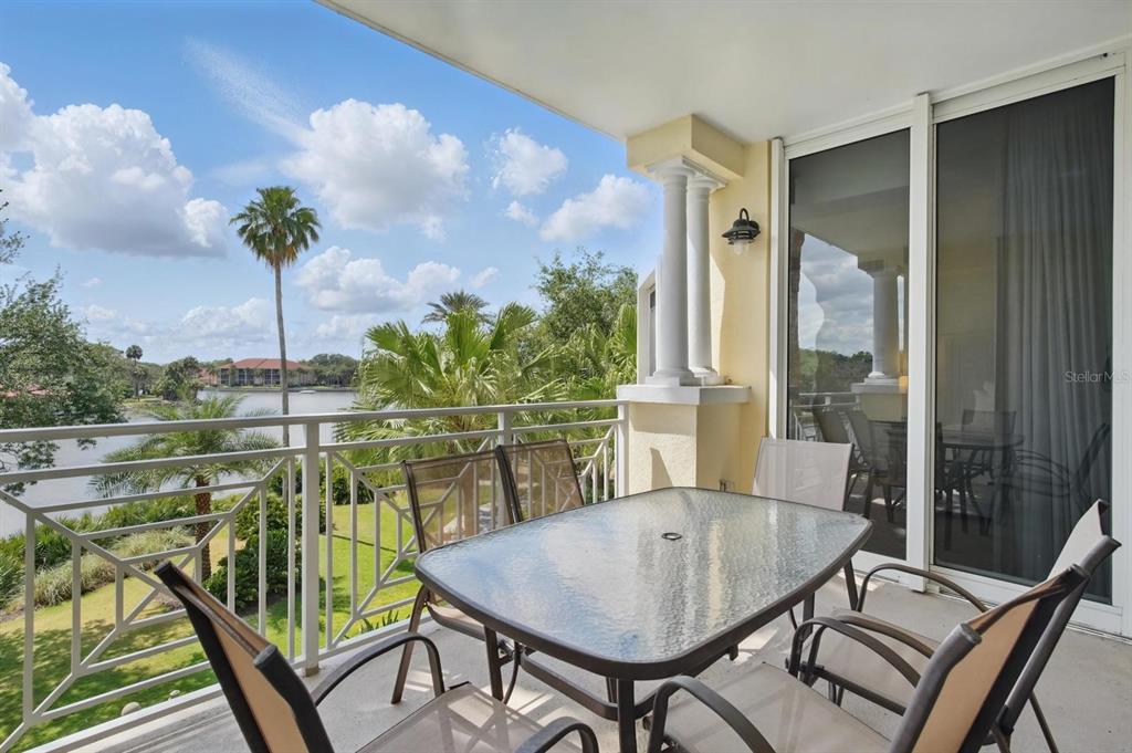 A balcony with a glass-topped table and chairs overlooks a lake and palm trees — 102 YACHT HARBOR DRIVE UNIT 263, PALM COAST, FL