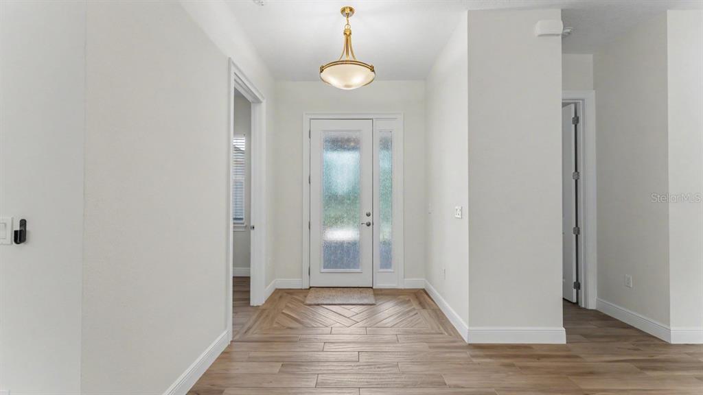 A bright entryway features wood-look tile flooring, a glass-paneled front door, and a pendant light — 5701 CRESTVIEW DRIVE, LADY LAKE, FL