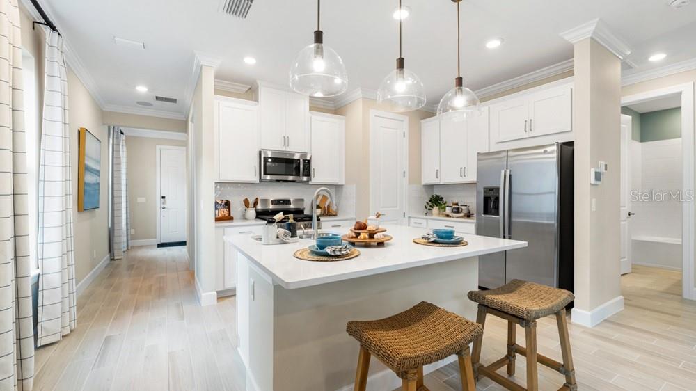 A modern kitchen features white cabinets, a large island with stools, and stainless steel appliances — 26937 LARK COURT, PUNTA GORDA, FL