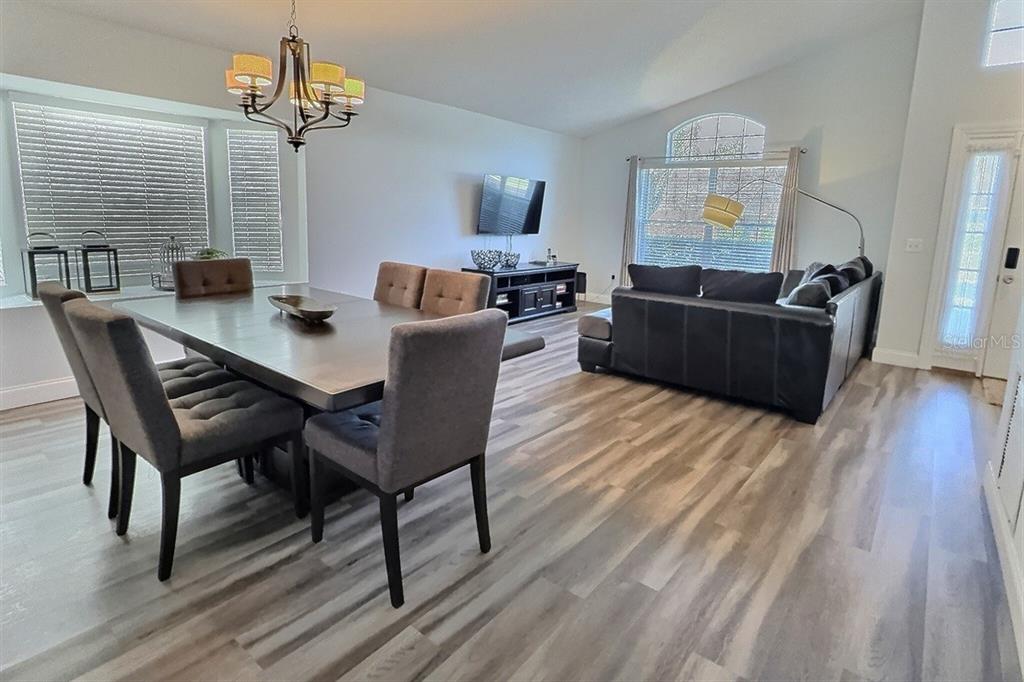 An open-concept living and dining area features wood-look flooring, a chandelier, and a sectional sofa — 1005 LAKE BERKLEY DRIVE, KISSIMMEE, FL