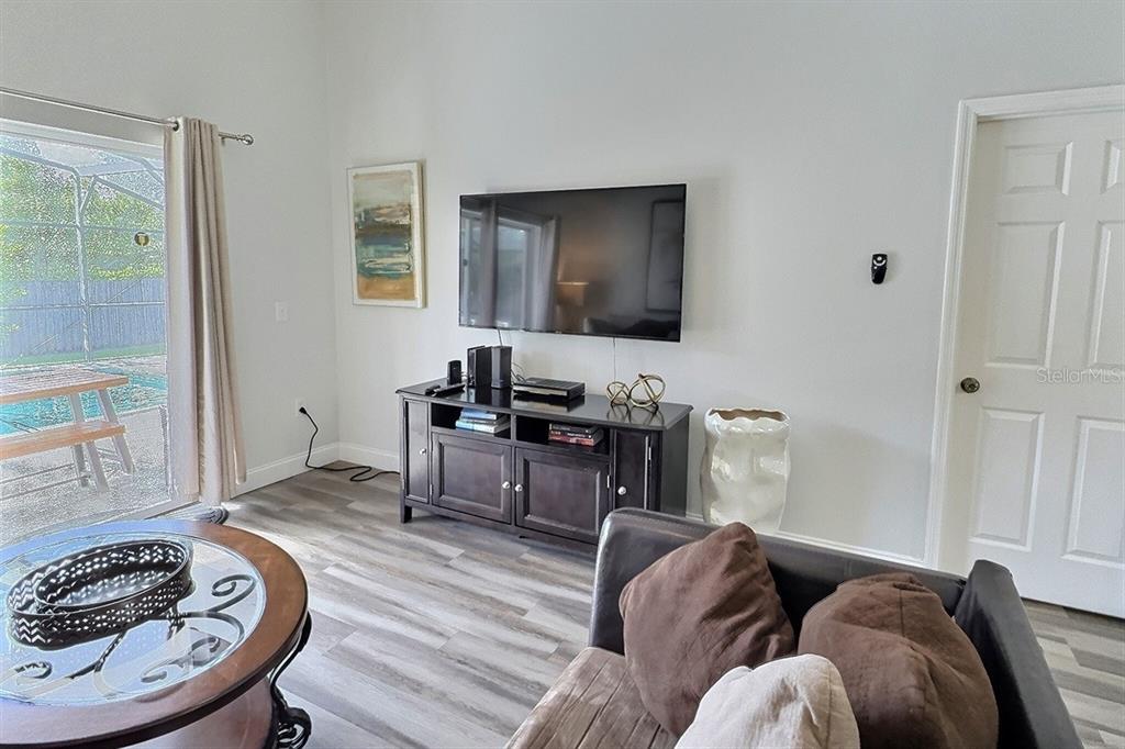 A living room features a wall-mounted television, a dark wood media console, and wood-look flooring — 1005 LAKE BERKLEY DRIVE, KISSIMMEE, FL