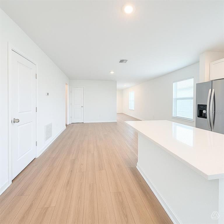 A bright kitchen with a white island and light wood-look flooring leads into a hallway — 13020 SASSAFRAS TRAIL, PARRISH, FL