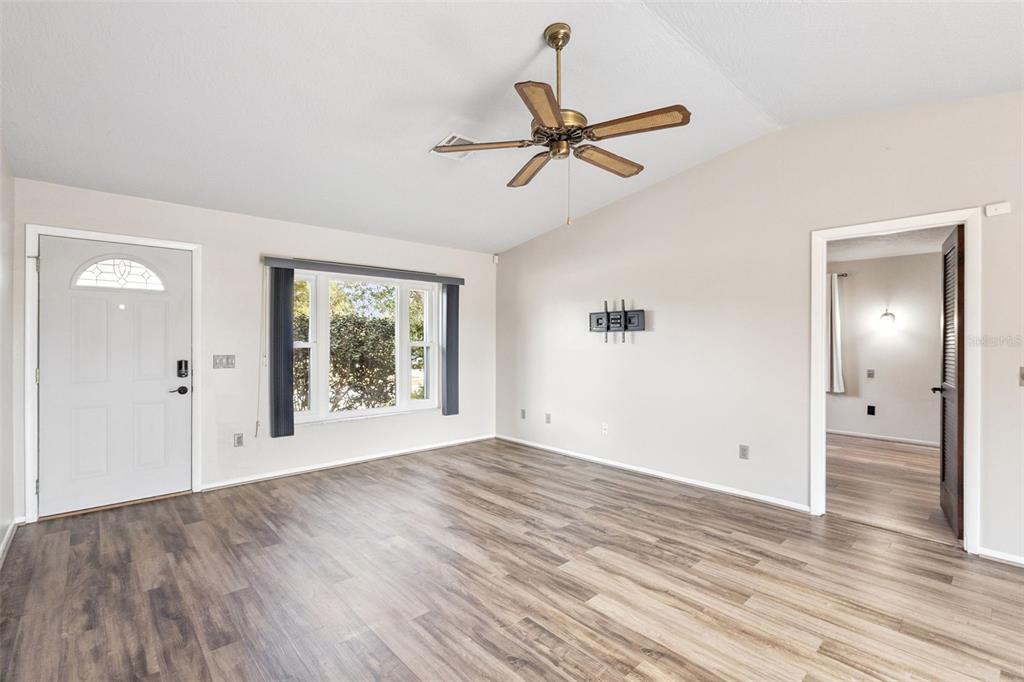 An empty living room features light-colored walls, wood-look flooring, a ceiling fan, and a window — 501 ANTOINETTE STREET, DELTONA, FL