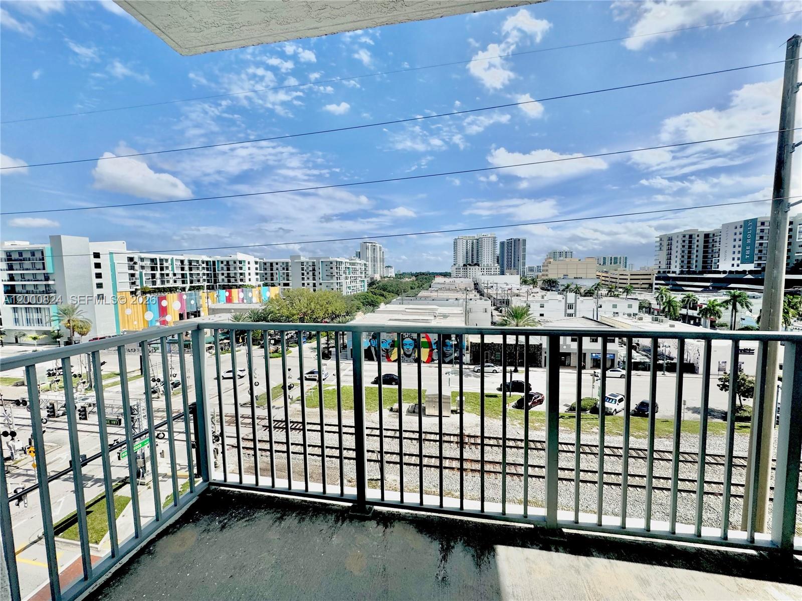 A balcony with metal railings overlooks a city street, railroad tracks, and surrounding apartment buildings — 140 S Dixie Hwy # 513, Hollywood FL 33020, HOLLYWOOD, FL