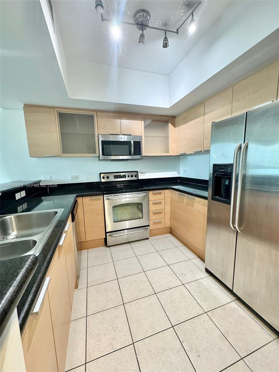 A kitchen features light wood cabinets, black countertops, stainless steel appliances, and tiled flooring — 140 S Dixie Hwy # 513, Hollywood FL 33020, HOLLYWOOD, FL