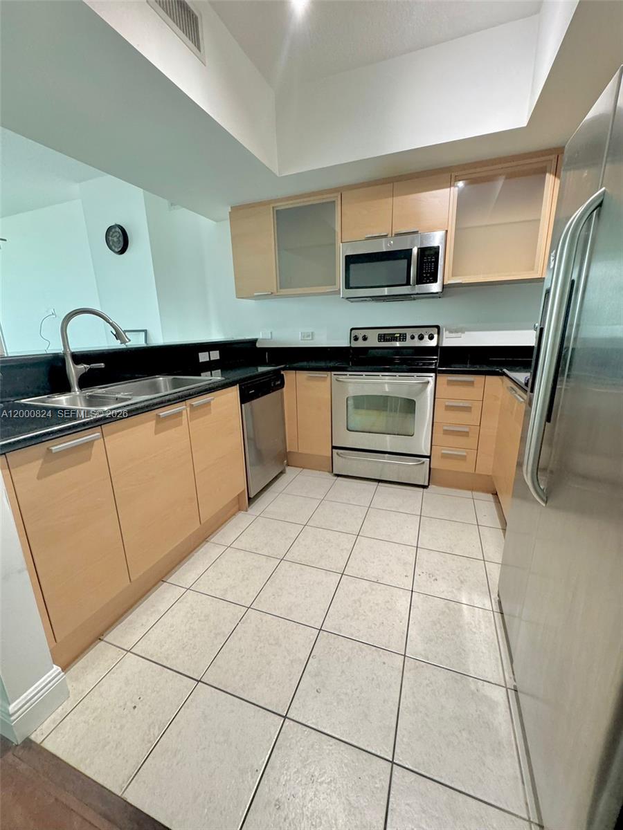 A kitchen features light wood cabinets, stainless steel appliances, and black countertops — 140 S Dixie Hwy # 513, Hollywood FL 33020, HOLLYWOOD, FL