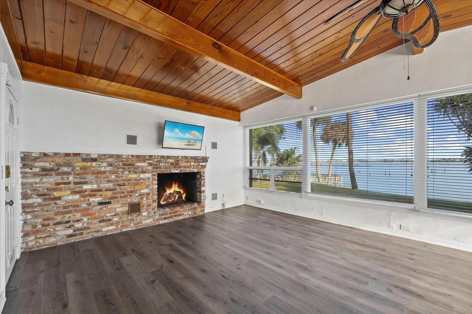 A living room features a brick fireplace, wood-plank ceiling, and large windows overlooking the water — 101 S Colorado Avenue, Stuart FL 34994, STUART, FL