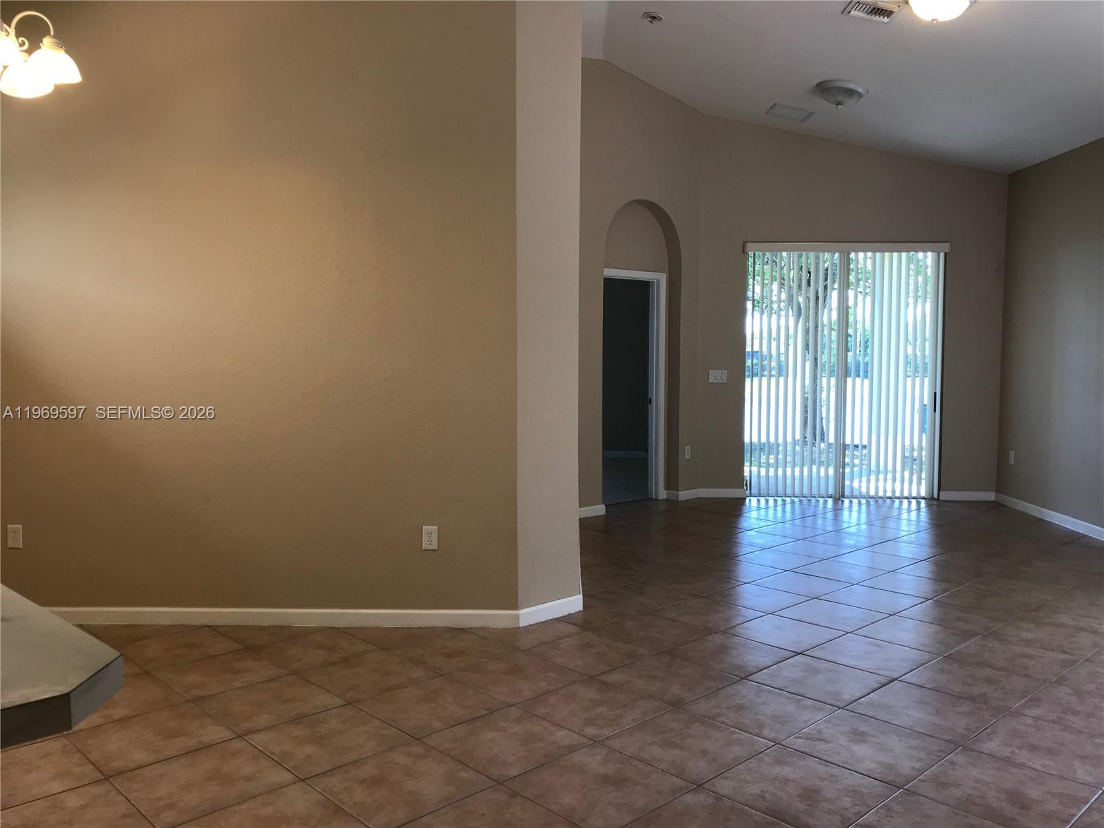 An interior view shows a tiled living area with beige walls and a sliding glass door — 3748 NE 9th Ct, Homestead FL 33033, HOMESTEAD, FL