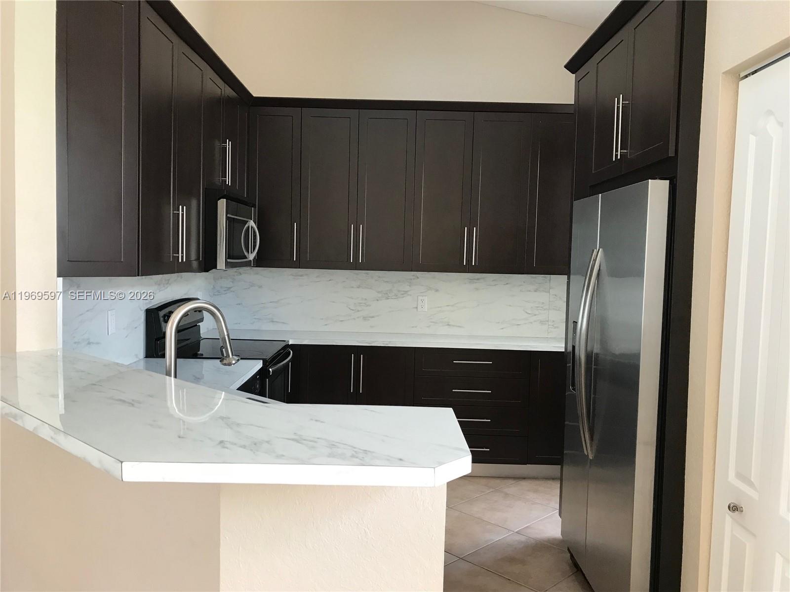 A kitchen features dark wood cabinets, stainless steel appliances, and white marble-patterned countertops — 3748 NE 9th Ct, Homestead FL 33033, HOMESTEAD, FL