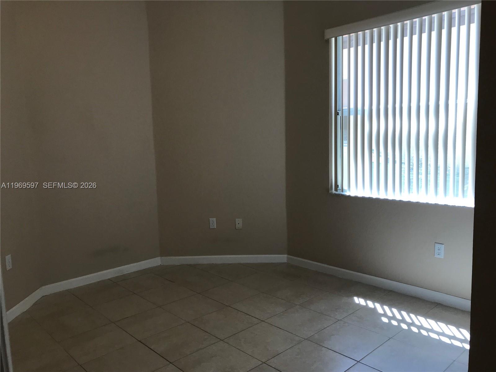 An empty room features beige walls, tile flooring, and a window with vertical blinds — 3748 NE 9th Ct, Homestead FL 33033, HOMESTEAD, FL