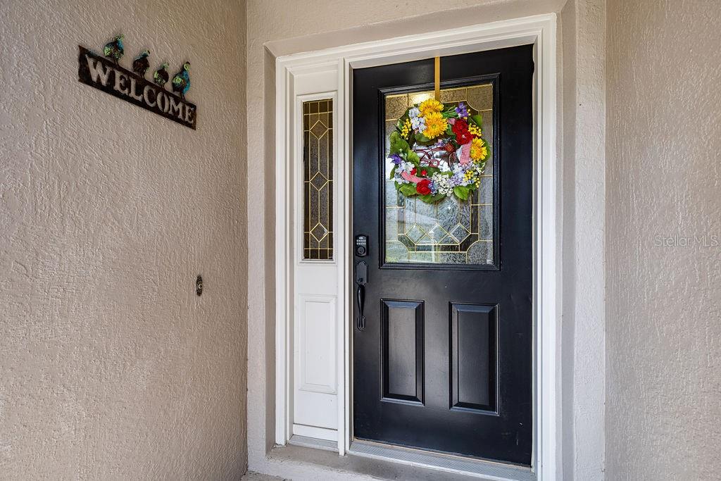 A black front door with a glass insert and a floral wreath sits in a stucco entryway — 6116 ARMADA STREET, TAVARES, FL