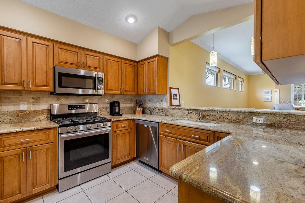 A kitchen with wood cabinets, granite countertops, stainless steel appliances, and light tile flooring — 6116 ARMADA STREET, TAVARES, FL